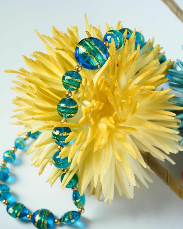 Close-up of a Murano necklace with vibrant blue beads featuring gold accents, displayed on a yellow decorative piece